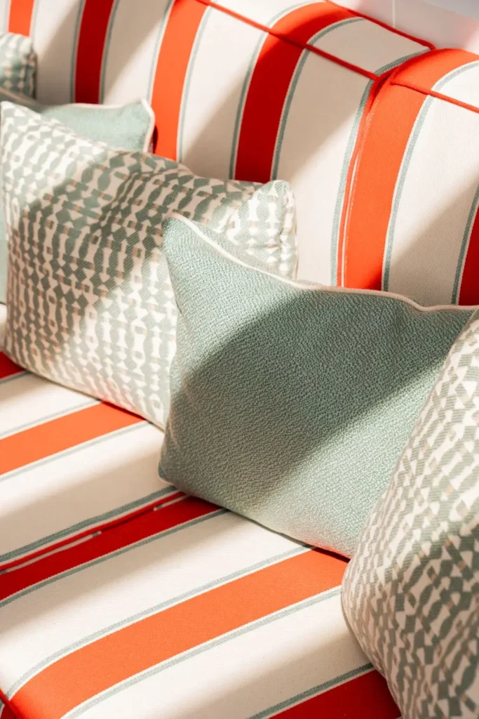 Gros plan sur des coussins vert d'eau texturés posés sur une banquette à larges rayures rouge et blanc