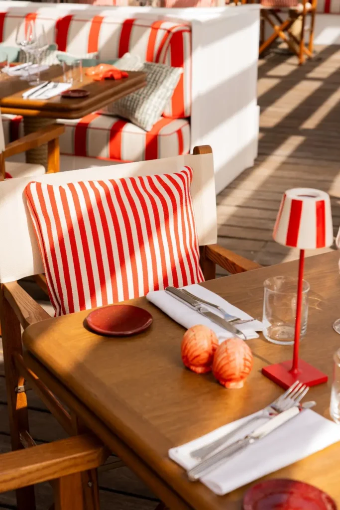 Couvert dressé sur table en bois avec coussin rayé rouge, salière terracotta et lampe de table rouge en terrasse