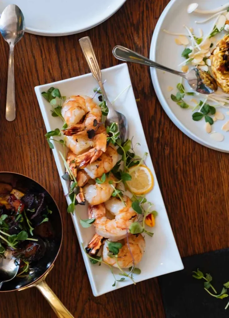 Assiette de crevettes grillées avec herbes fraîches et citron, entourée de moules marinières et d'un plat de fruits de mer