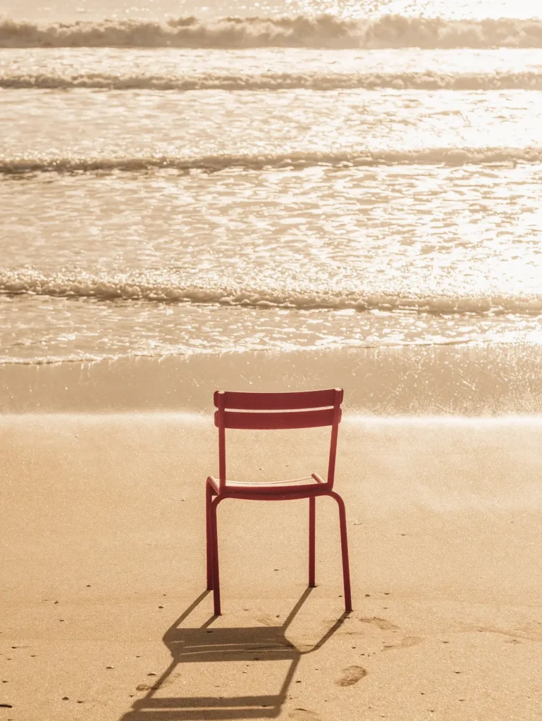 Chaise de bistrot rouge seule posée sur le sable face aux vagues, lumière dorée de fin de journée à La Baule