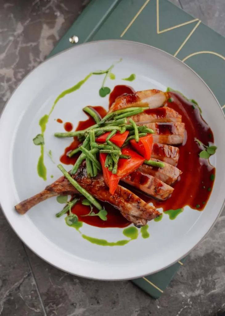 Magret de canard tranché en éventail avec sauce rouge, haricots verts et poivron sur assiette blanche