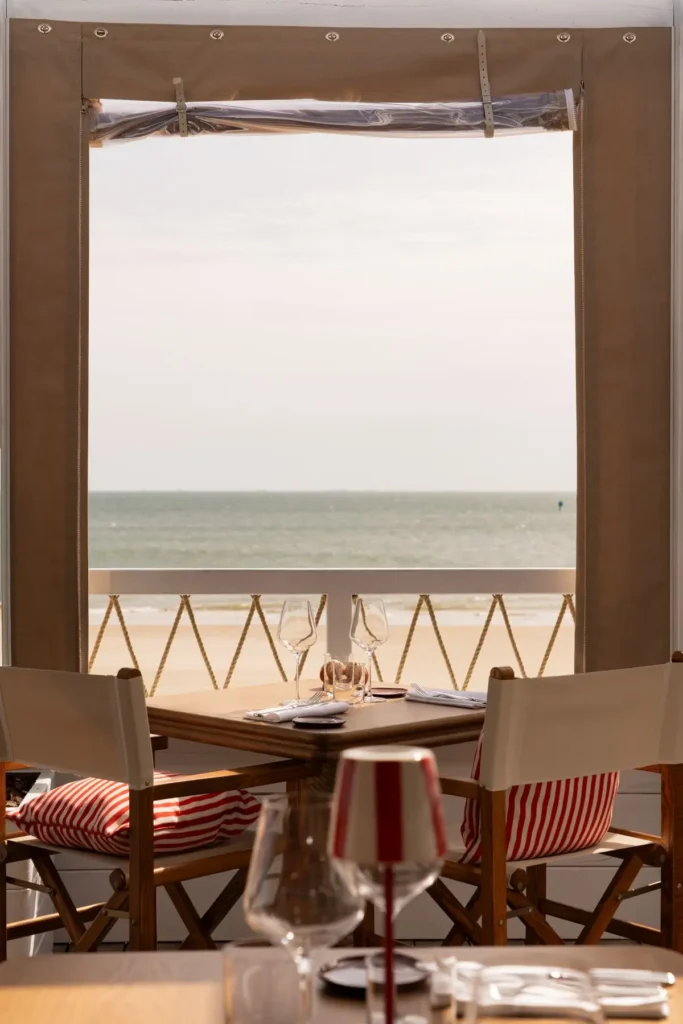 Table dressée pour deux avec verres à vin, vue directe sur la plage et l'océan depuis la terrasse du restaurant